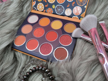 A side angle of Bold and Luscious Cosmetics orange themed eye shadow palette with 12 colors on it. the oranges range from dark orange which is almost brown to colors closer to peach and yellow. there are shimmer colors. 