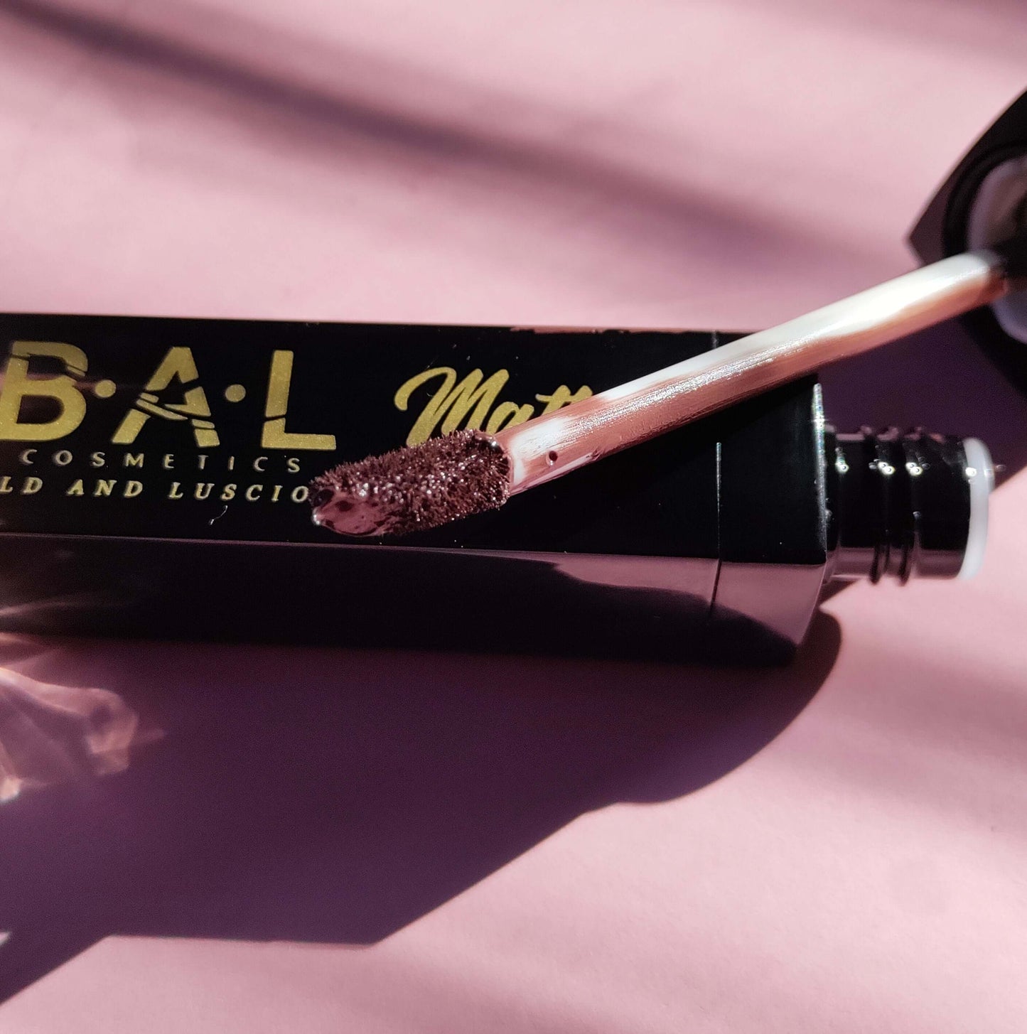 Close up of the wand for color cooca which is our creamiest richest chocolate brown color. The wand of the liquid lipstick is resting on the black bottle with the Bold and Luscious Cosmetics Label visible. 