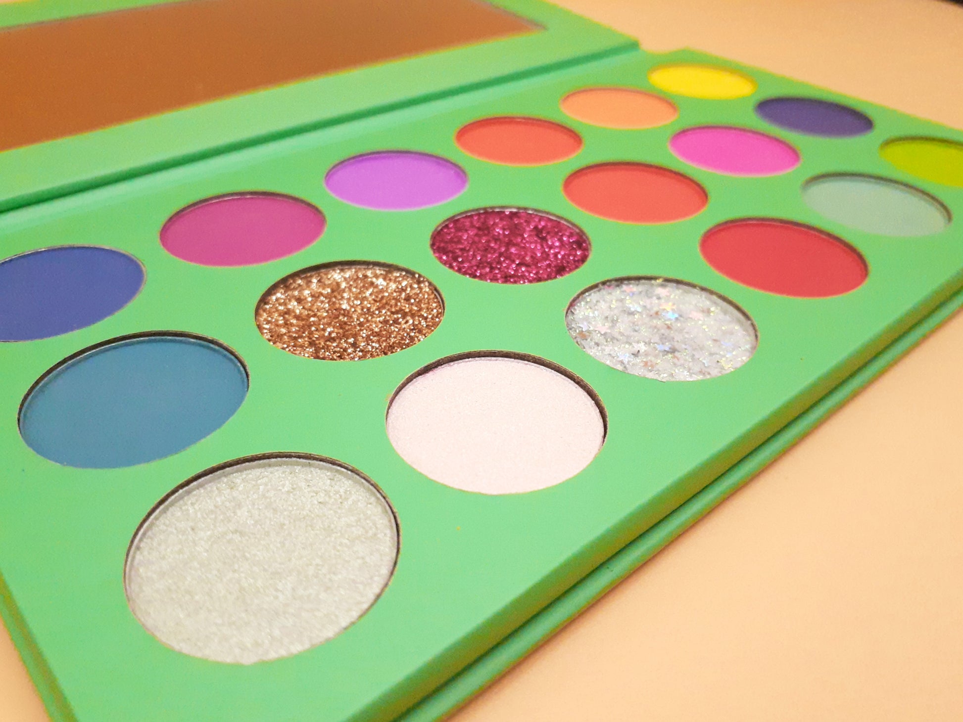 a close up view of the palette reveals the texture in the glitter pans. A mirror inside the palette is visible in the top of the photo.
