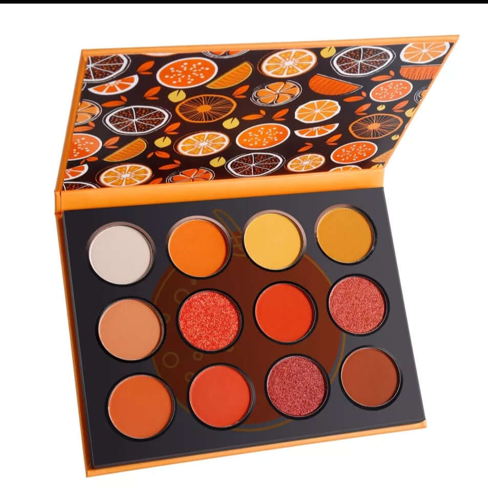 a front view of the inside of the eye palette. the top of the palette features orange slices as decoration.  The palette has very pigmented oranges and yellows inside.