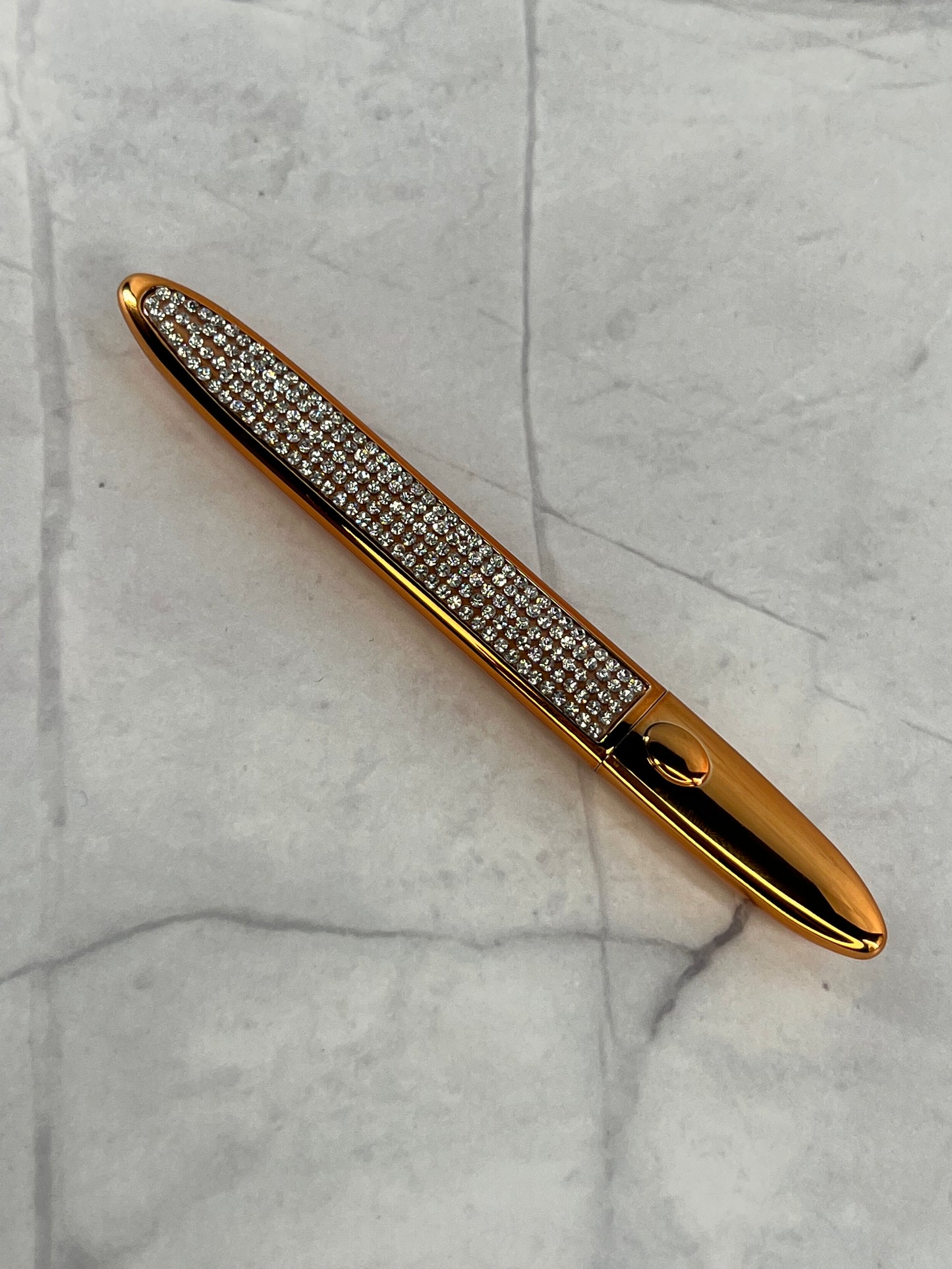 Bold and Luscious Diamond Status Magic Lash Adhesive Liner is a flat and wide style pen casing with a fine tip for precision use. a full shot reveals the beautiful casing with white daux diamonds in a straight line on the outside and a gold trim.