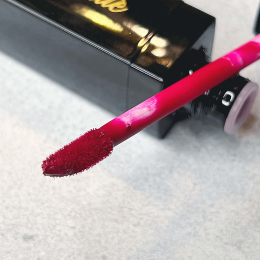 a  close up of a brush with fuchsia color with red undertone. It rests on the neck of the Bold and Luscious Brand Bottle. 