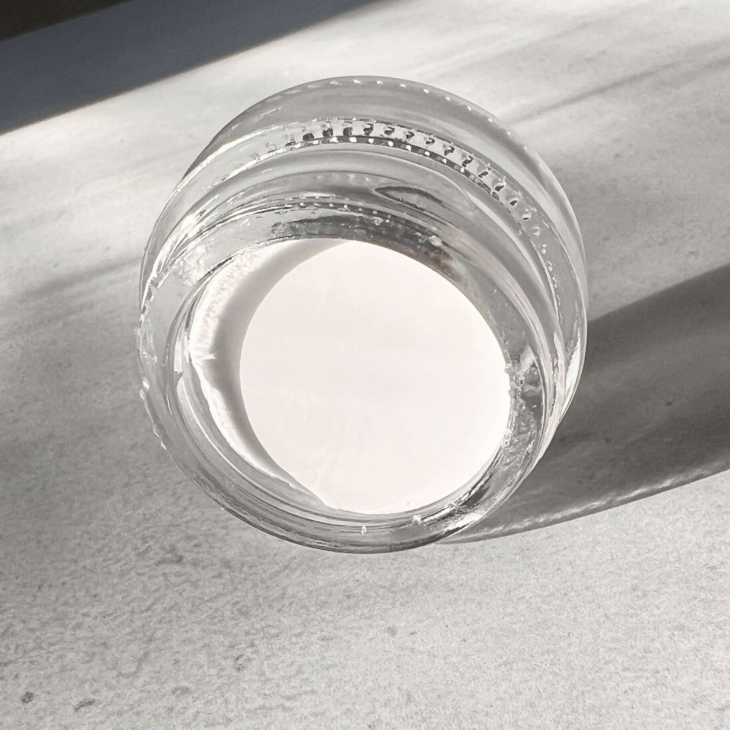 Creamy gel eyeliner in a glass pot rests on its side. This position shows you that the white eyeliner is creamy and thick.