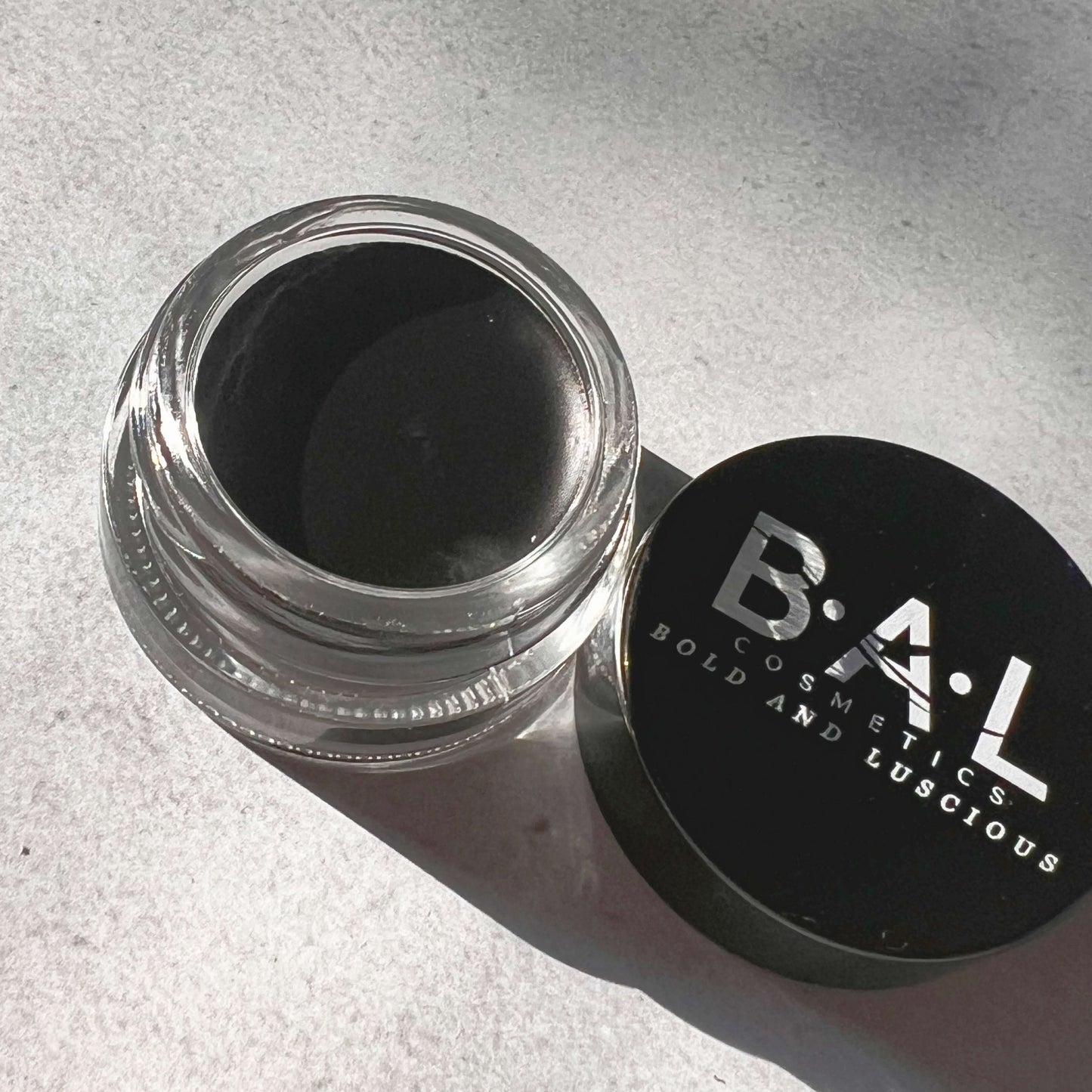 Black Gel Eyeliner in a small glass pot. the Logo for Bold and Luscious Cosmetics is visible on the lid. The texture is soft and creamy.