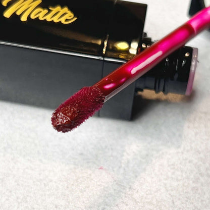 The lip wand rests on the the neck of the bottle for the bold and luscious liquid lipstick sugar plum. this color is a rich burgundy.
