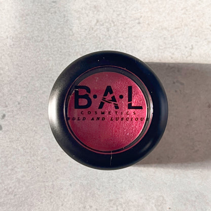 A closed photo of a shimmery red eye color. the color is shimmery, and the Bold and Luscious Cosmetics Logo is visible on the front.