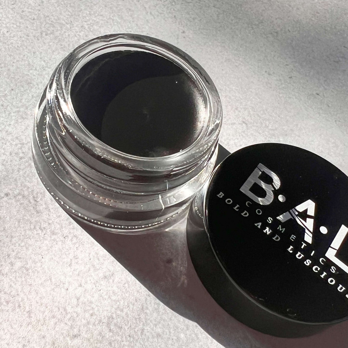Black Gel Eyeliner in a small  glass pot. the Logo for Bold and Luscious Cosmetics is visible on the lid. The texture is soft and creamy.