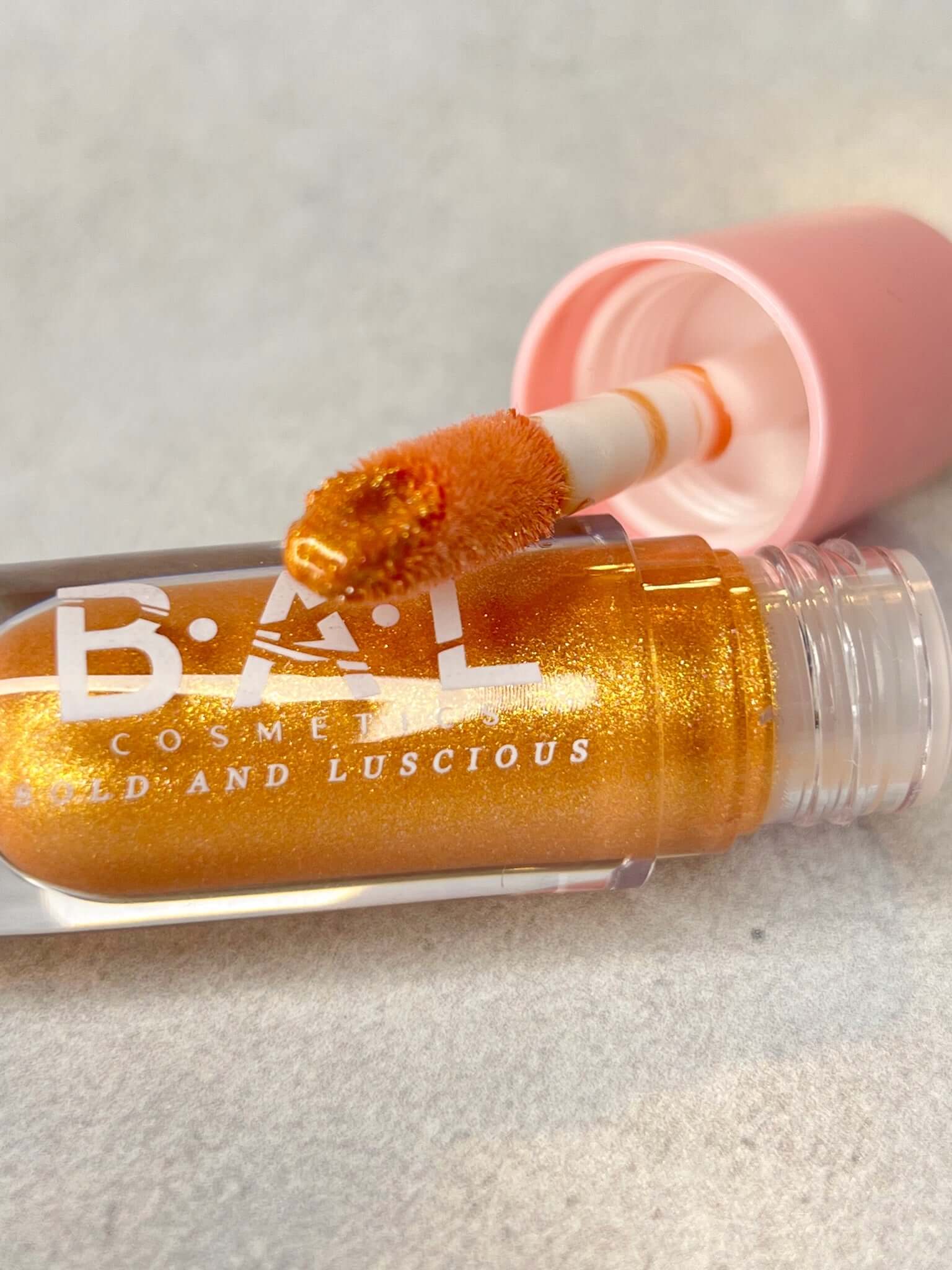 The bottle of champagne Glassy Gloss is laying on its side showing all of the detail in the color.  The color is gold with gold glitter. 