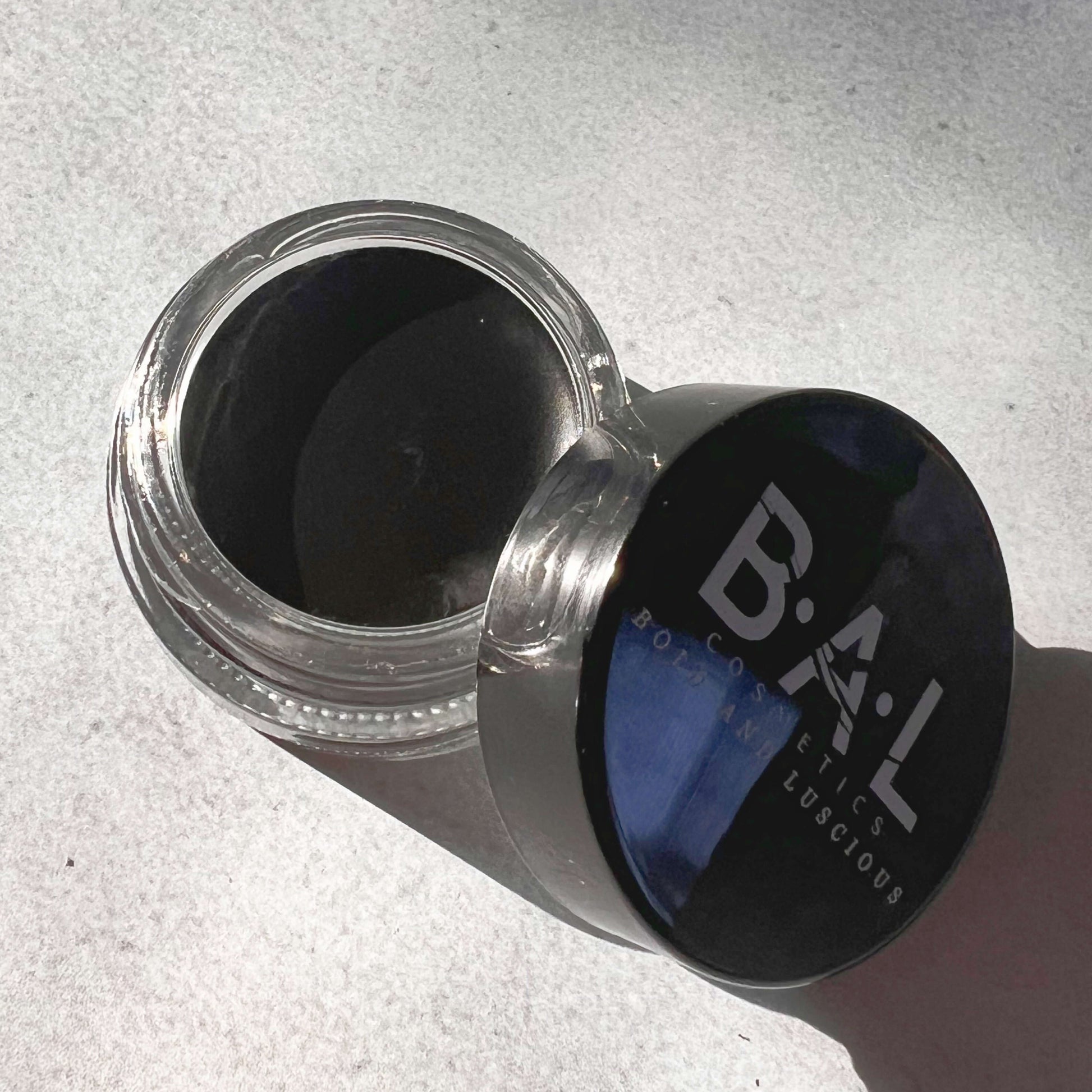 Top View of Gel Eyeliner black in a  glass pot. the Logo for Bold and Luscious Cosmetics is visible on the lid. The texture is soft and creamy.