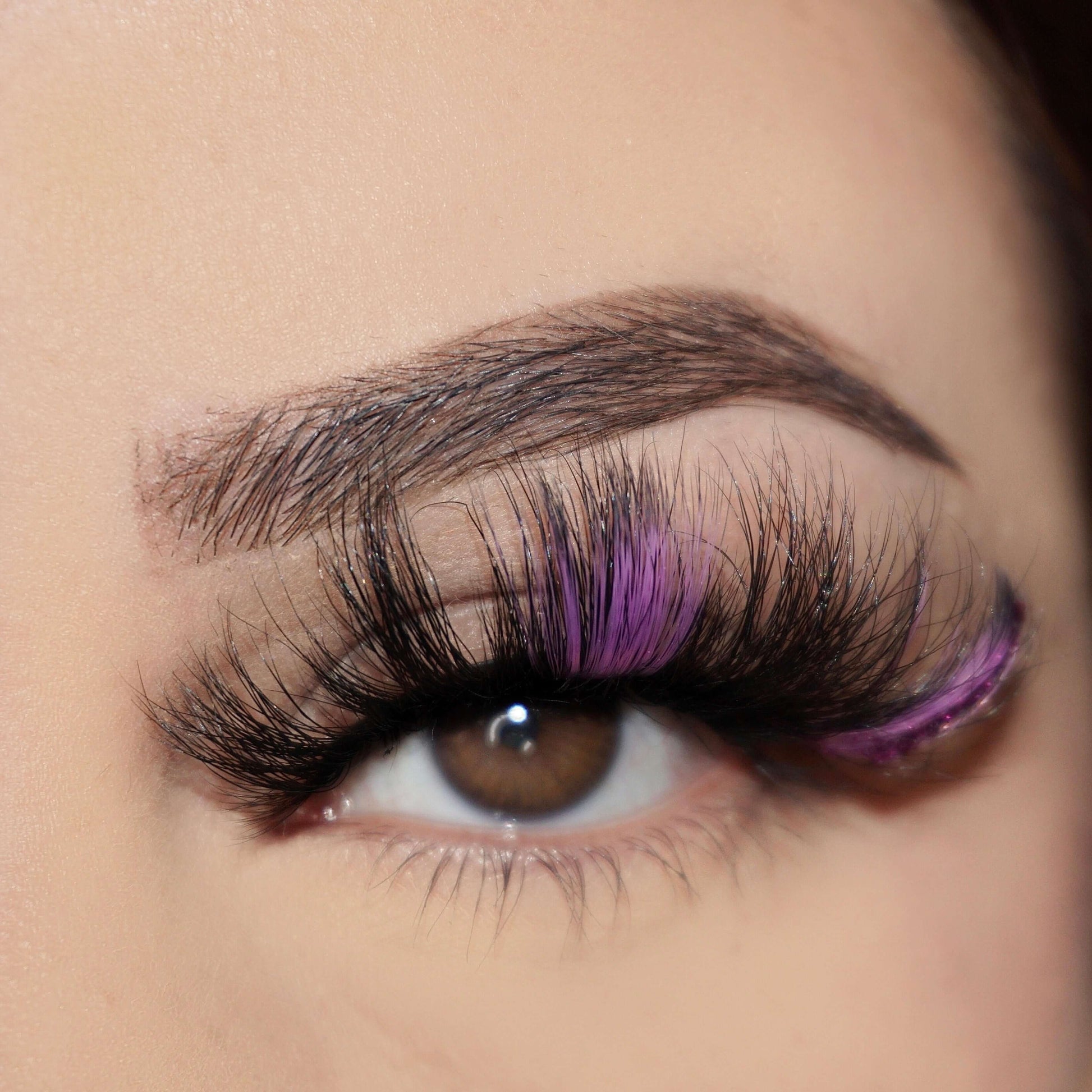 A close up Picture of Bold and Luscious Color Splash Lashes when affixed to an eye. This style is Misha. You can see it begins with black lashes, then has purple lashes, then another patch of black lashes followed by purple with a glitter strip closer to the outer crease of the eye.